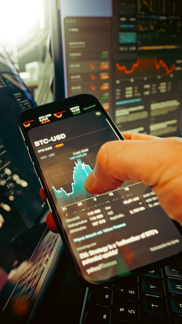 hero-img-01 Une main tient un smartphone affichant le graphique BTC-USD au milieu d’écrans de trading numériques, mettant en avant la finance crypto.